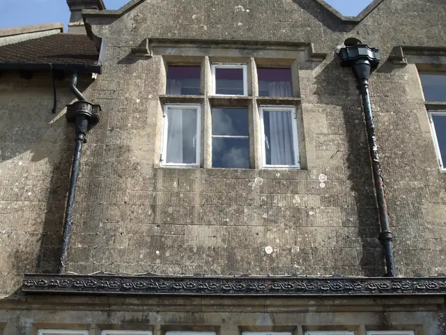 Black cast iron gutter, hopper heads and downpipes on a stone building.