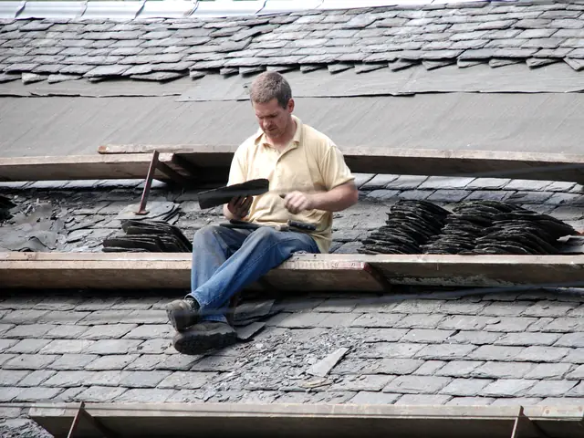 A roofer sitting on battens, dressing slates by hand on a roof being re-slated.