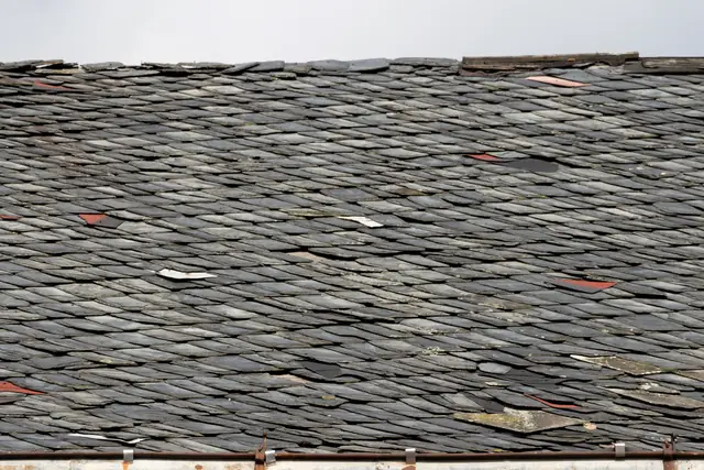 Close view of a weathered slate roof with individual slates replaced.