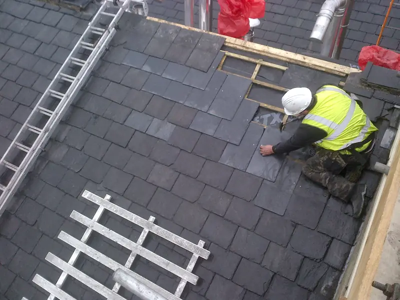 A roofer in a hi-vis vest laying new natural slate, seen from above.